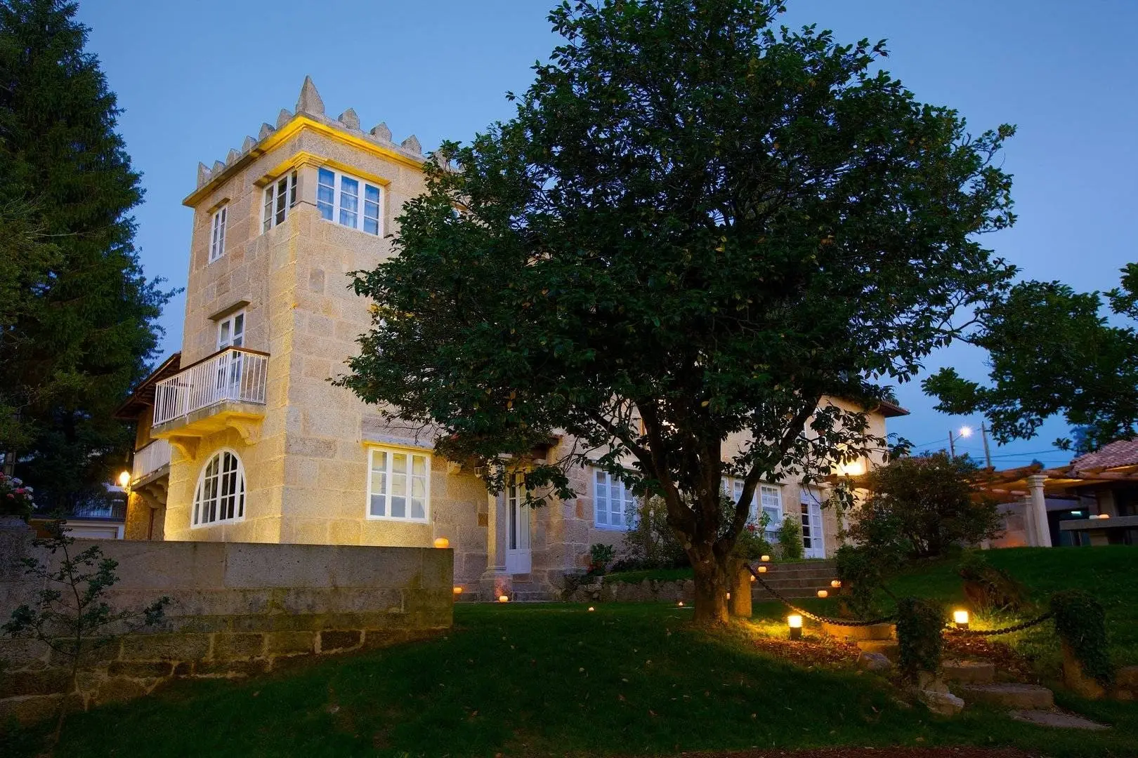 The casona’s crenellated tower against an open sky, its stone façade lit and the garden lights glowing